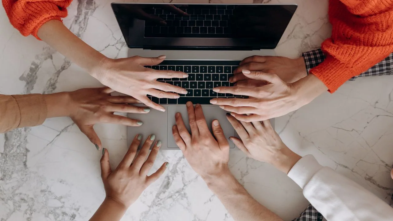 Hands working together around a laptop.