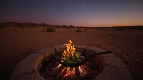 Food cooking over an open fire in a desert setting.
